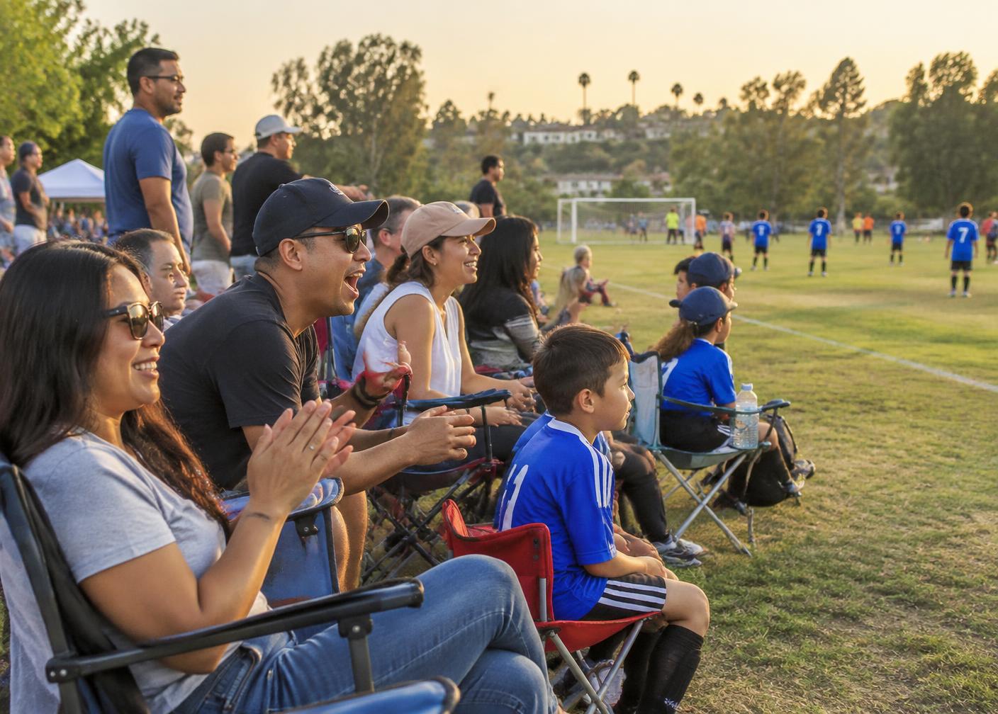 Parents and families cheering from the sideline of a youth soccer game in Orange County